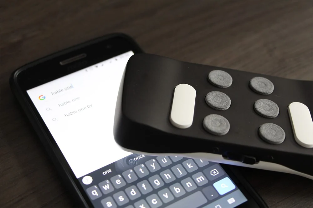 Hable One-controller naast een smartphone met een geopend tekstscherm.