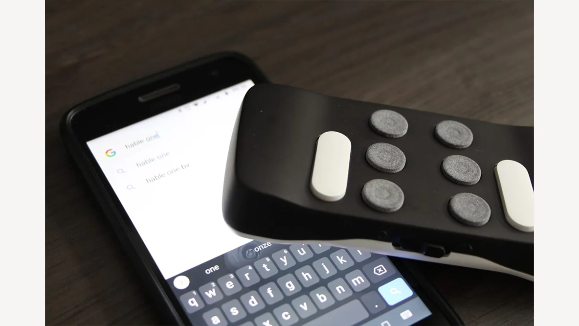 Hable One-controller naast een smartphone met een geopend tekstscherm.