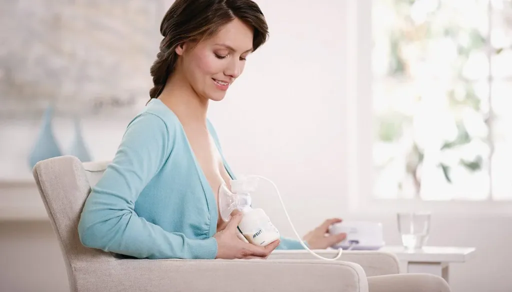 A woman uses a Philips Avent breast pump while sitting on a sofa.