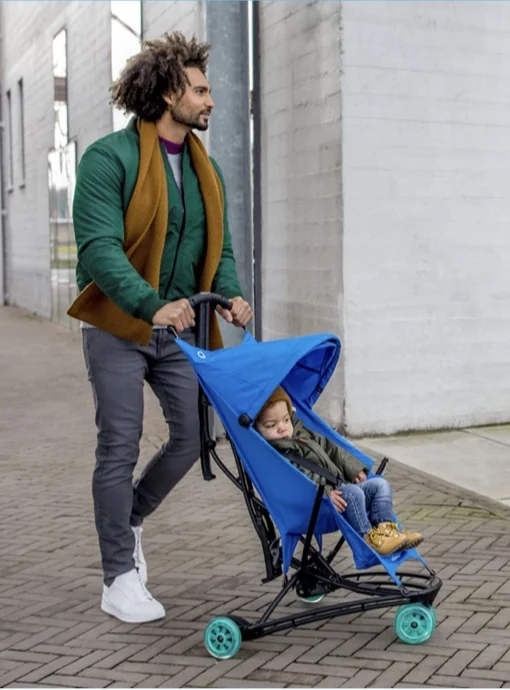 A parent pushes a blue Quinny Yezz with a child down a street.