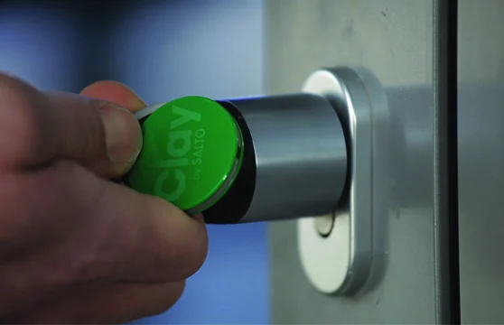 A green Clay tag held against an electronic door lock.