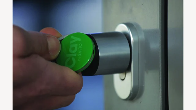 A green Clay tag held against an electronic door lock.