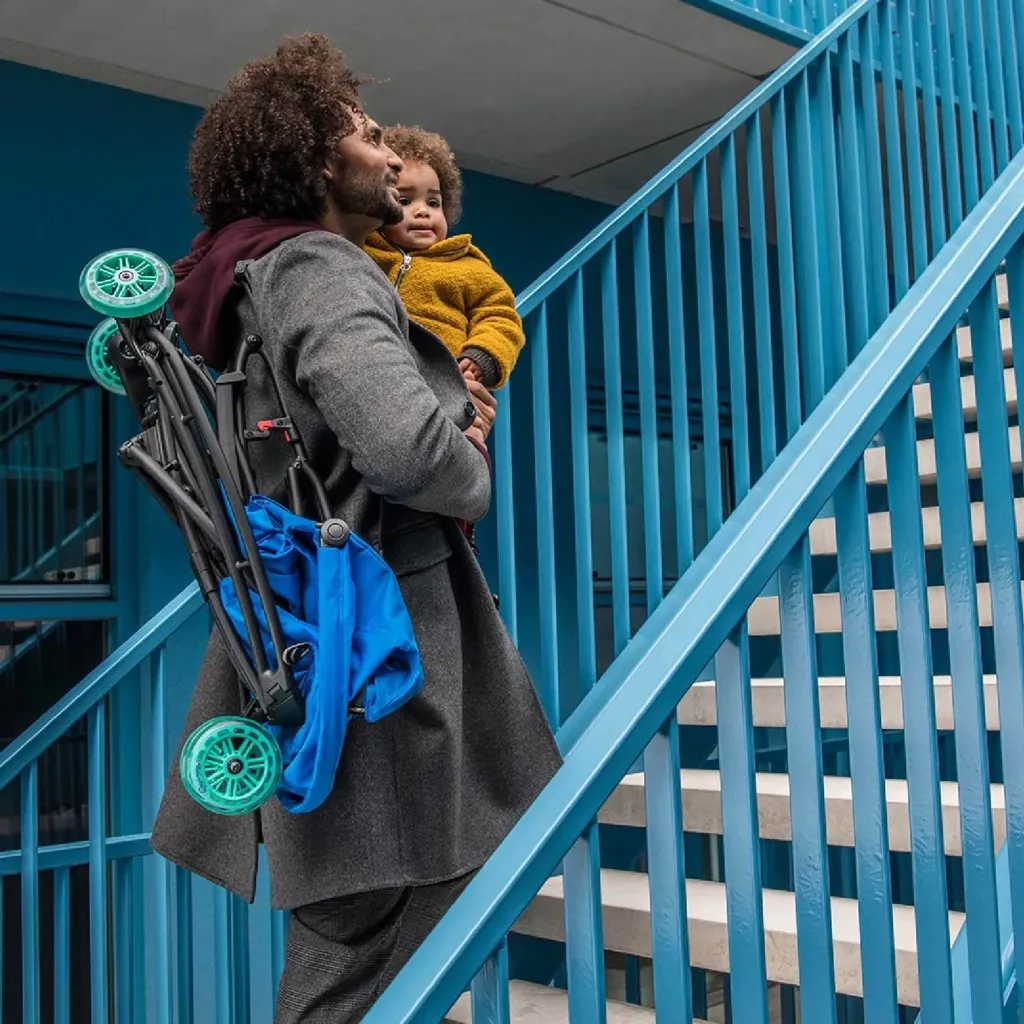 A parent carries a child and a folded Quinny Yezz on a staircase.