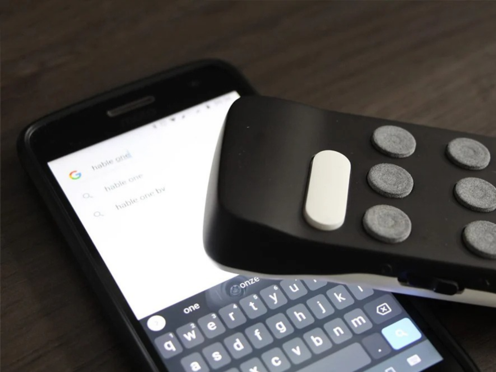 Hable One-controller naast een smartphone met een geopend tekstscherm.